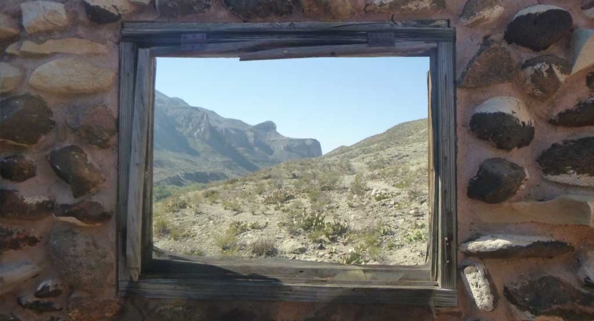 From inside a stone structure, a window frames the vast desert landscape beyond. 